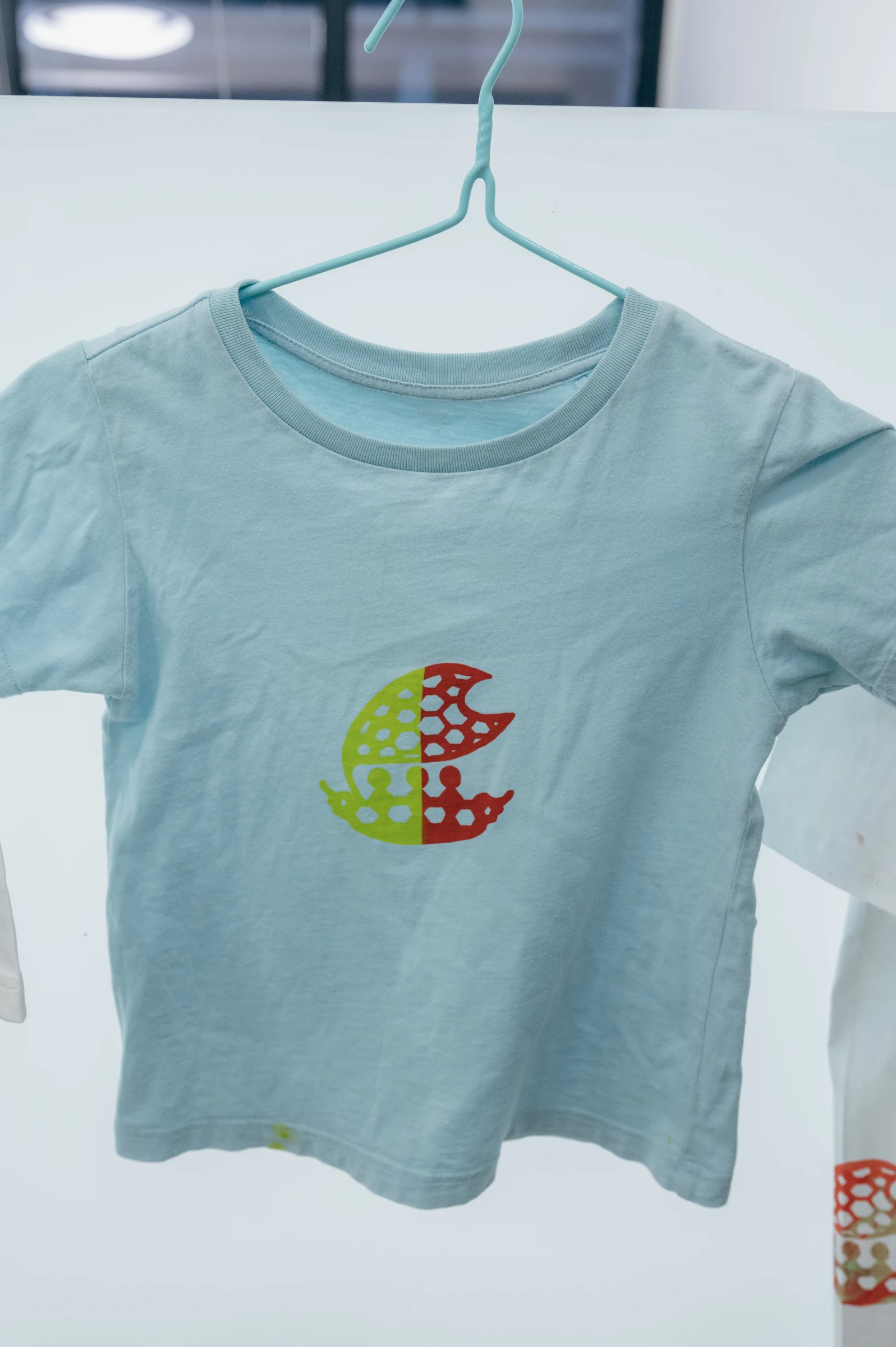 淺藍色 T-shirt 上印著紅綠雙色船帆圖樣
